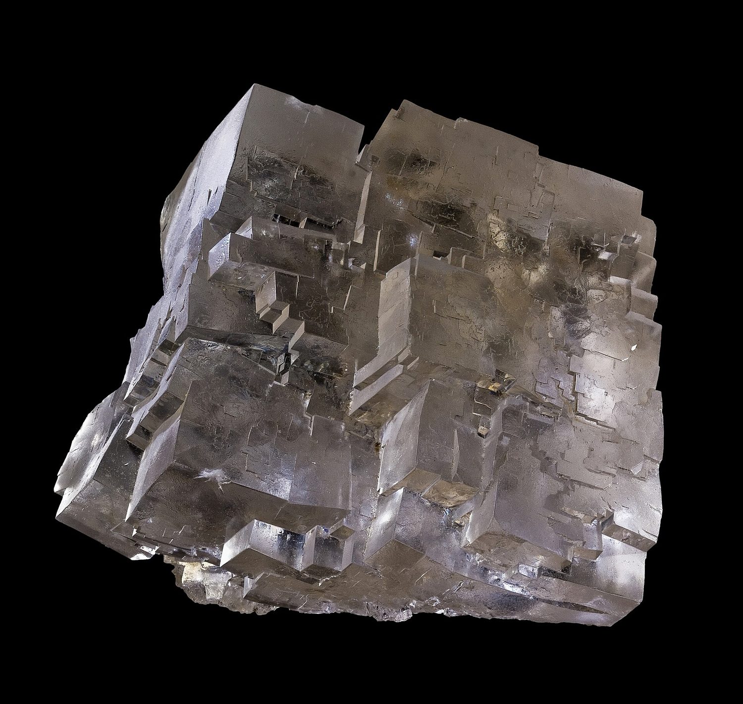 A clear-grey rock salt crystal on a black background, made of many small cube-shaped blocks with right-angled faces