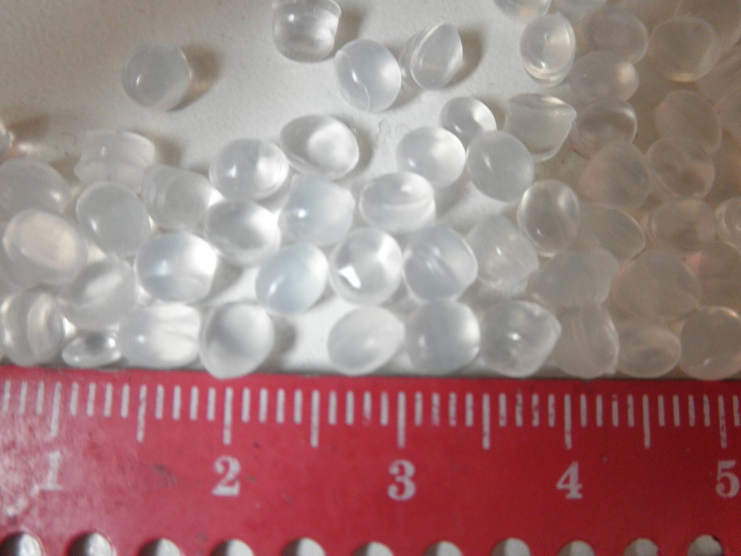 A pile of small translucent poly(ethene) pellets next to a ruler showing they are a few millimetres across