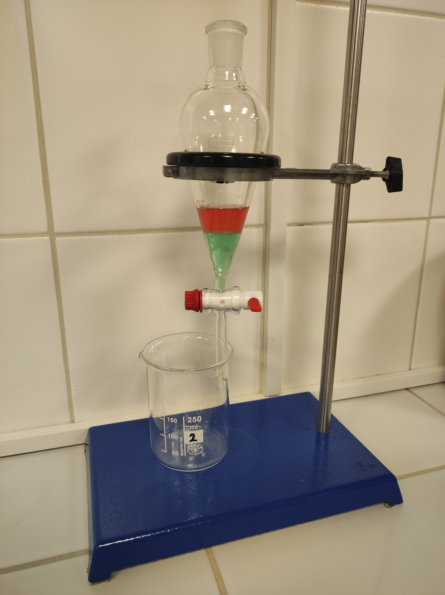 Un embudo de decantación sujeto sobre un vaso, conteniendo dos capas líquidas de color diferente que no se mezclan