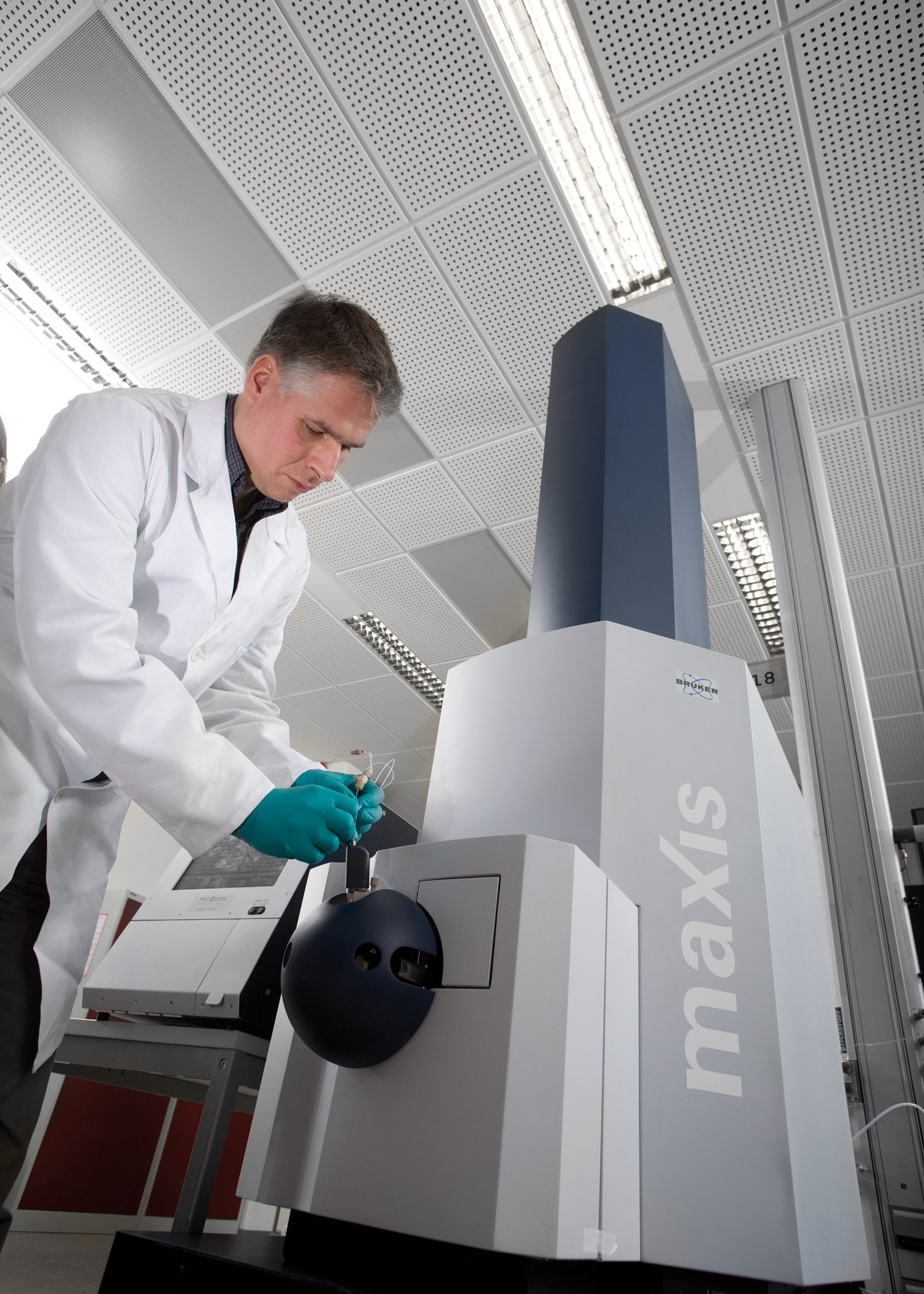 A scientist in a laboratory loading a small sample into a large modern mass spectrometer