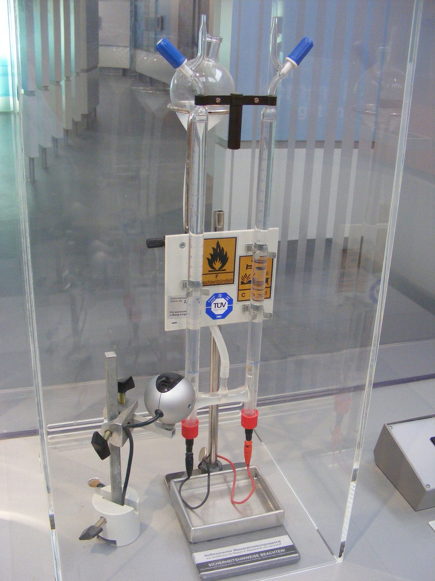 A glass Hofmann voltameter on a stand, wired to a power supply, with a gas-collection tube on each side