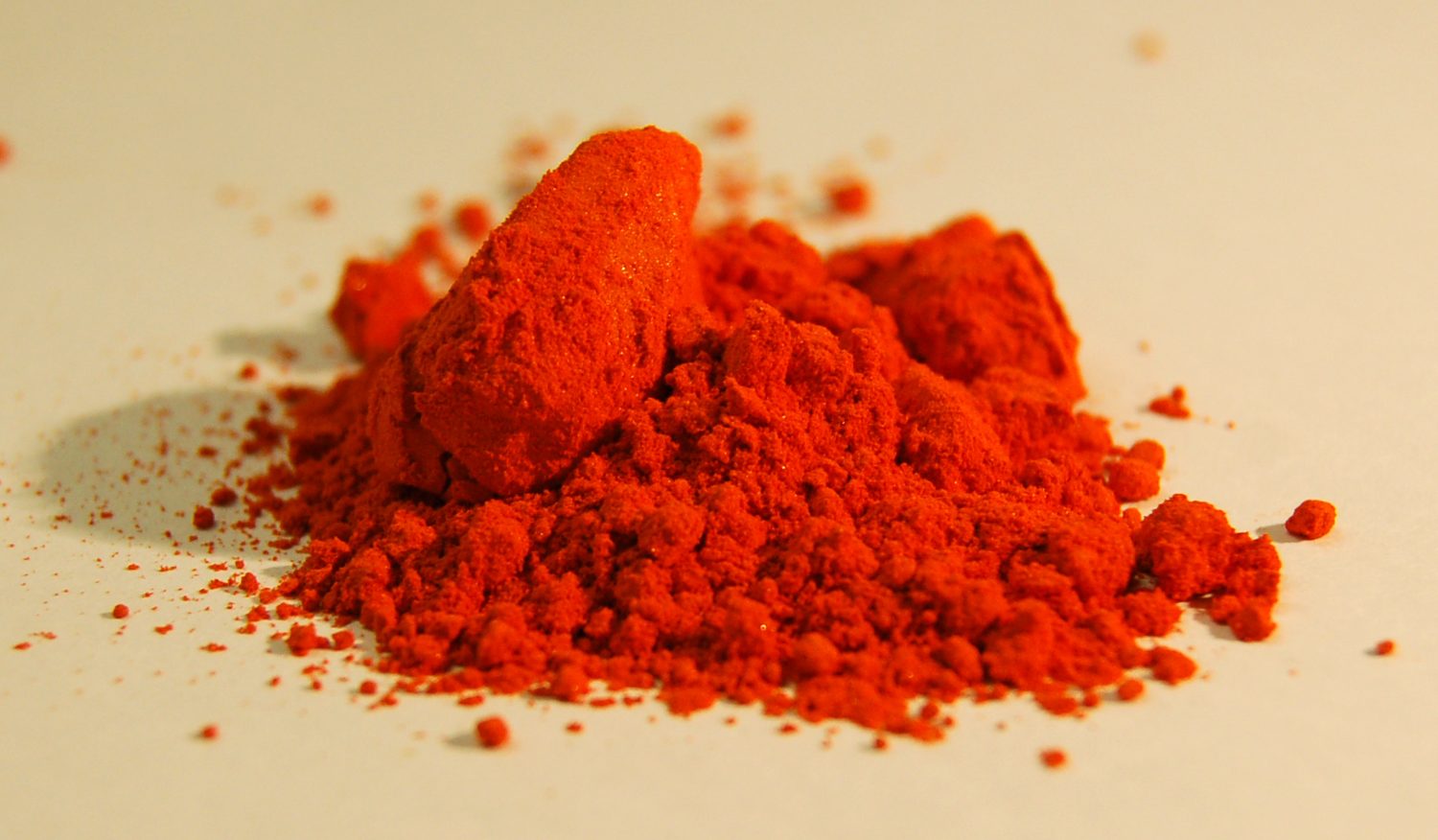 A small pile of bright orange methyl orange dye powder on a pale background