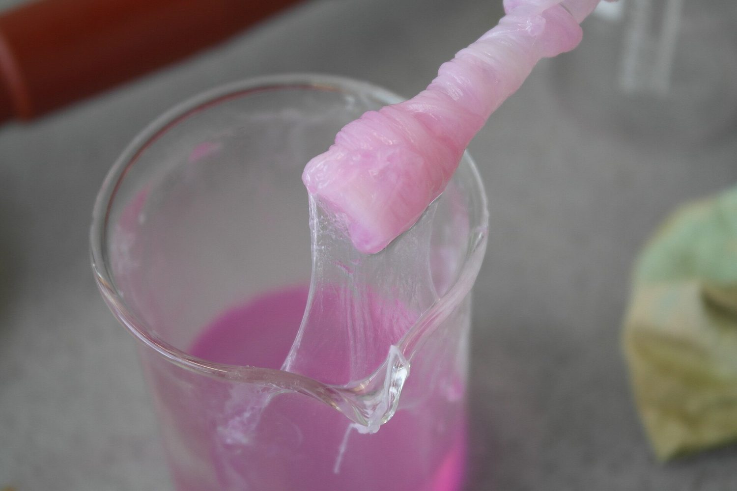 A pink strand of nylon being pulled up out of a beaker, forming a continuous thread at the surface of the liquid