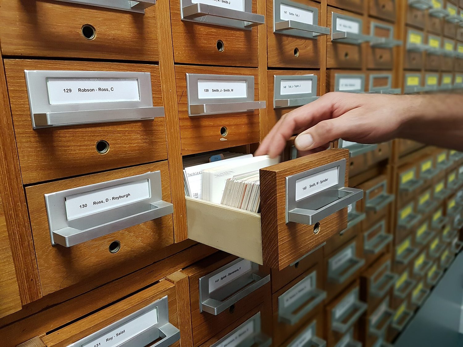A hand searching a card-index filing cabinet