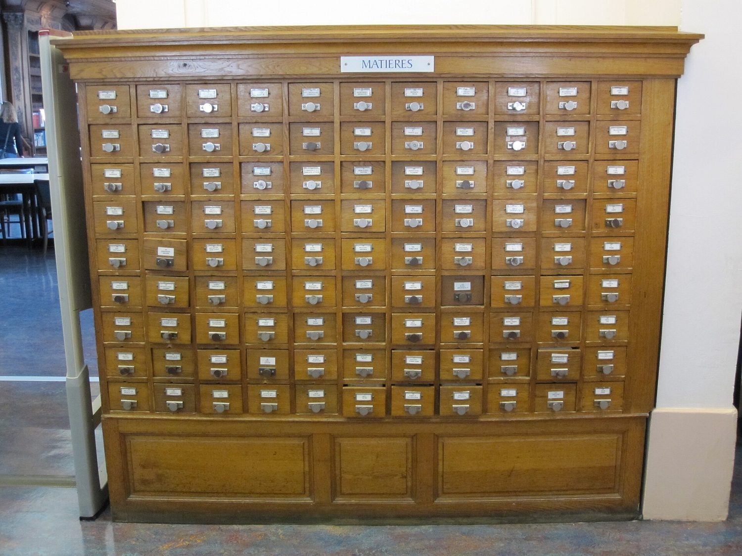Un catálogo de tarjetas de biblioteca: una pared de pequeños cajones de madera, uno abierto para mostrar las tarjetas archivadas en orden