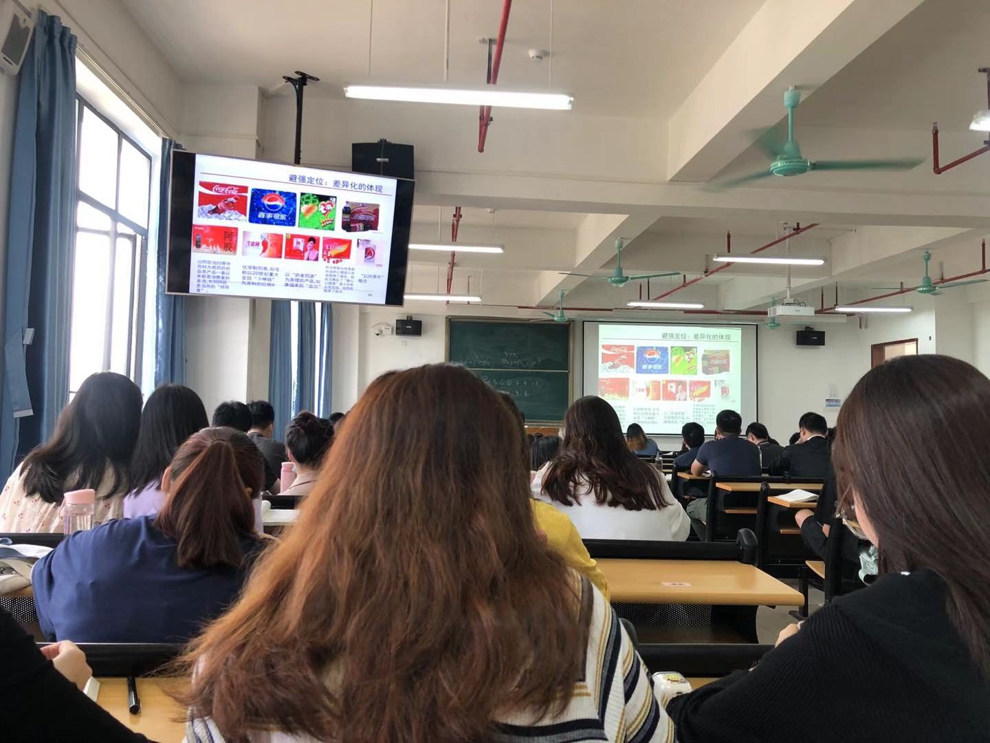 A modern lecture room full of students facing a large screen and a teacher