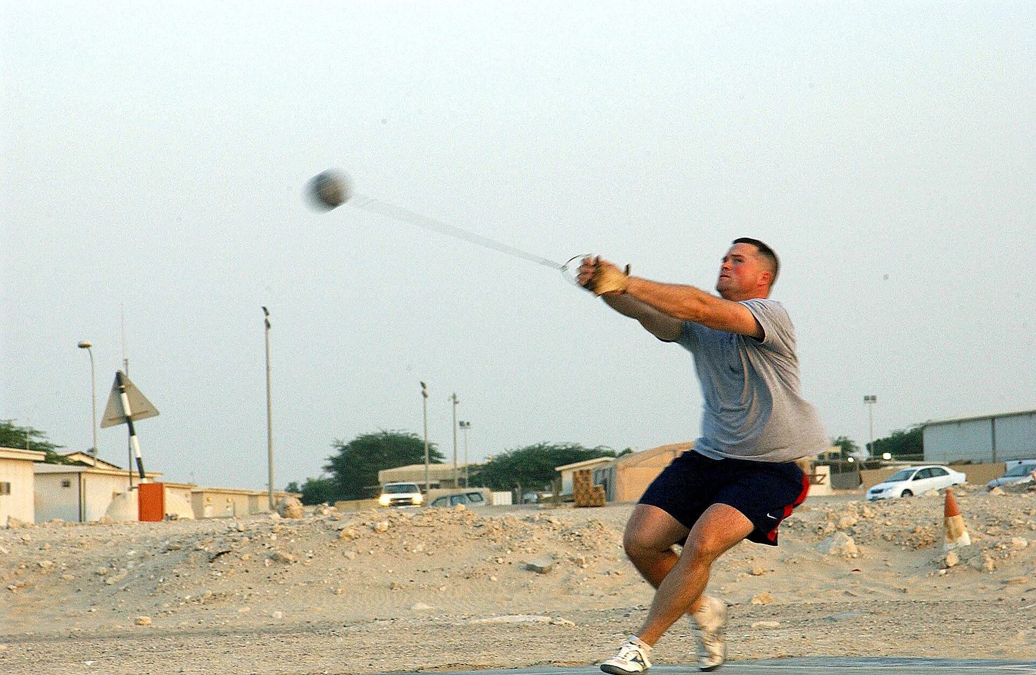 An athlete spinning, swinging a hammer on a taut wire out to one side, the ball blurred by its speed