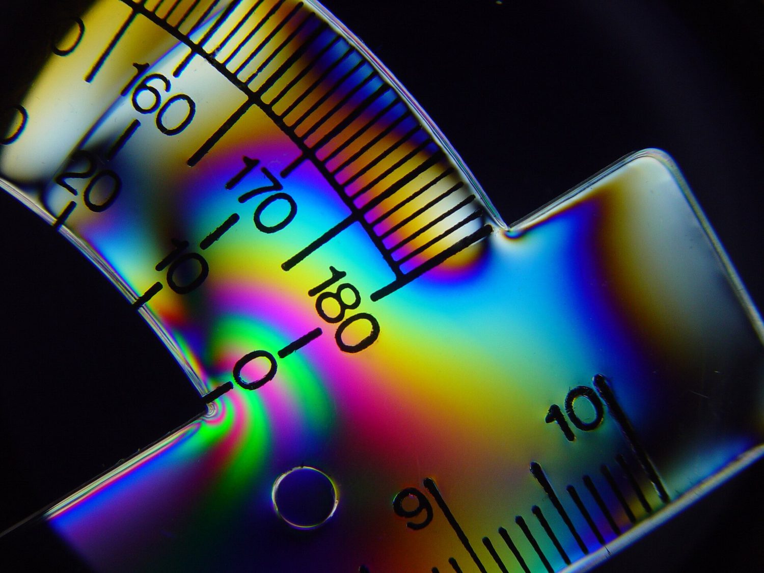 A clear plastic protractor glowing with bands of rainbow colour against a black background