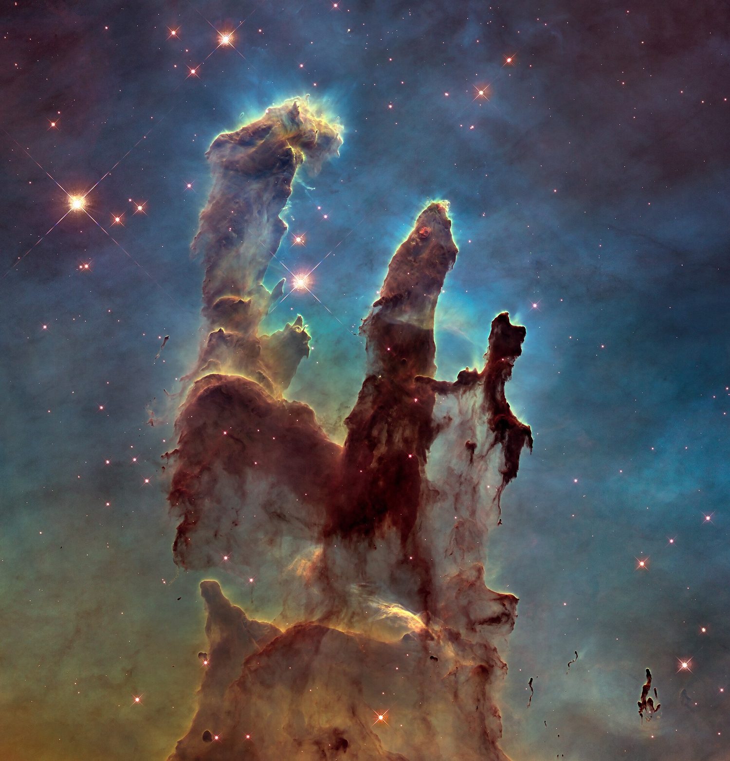 Ba cột khí và bụi màu nâu vàng vươn cao trước nền tinh vân màu xanh lục lam, được coronal bởi những ngôi sao trẻ sáng và các điểm sáng rải rác