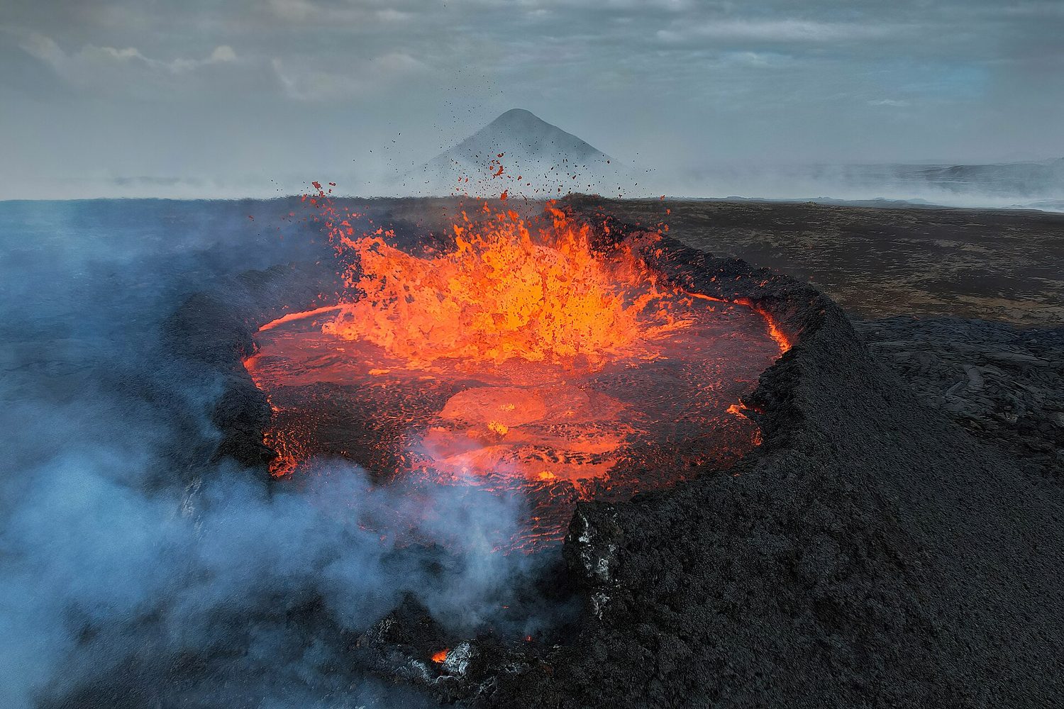 Bright orange molten lava fountaining out of a dark volcanic crater in Iceland