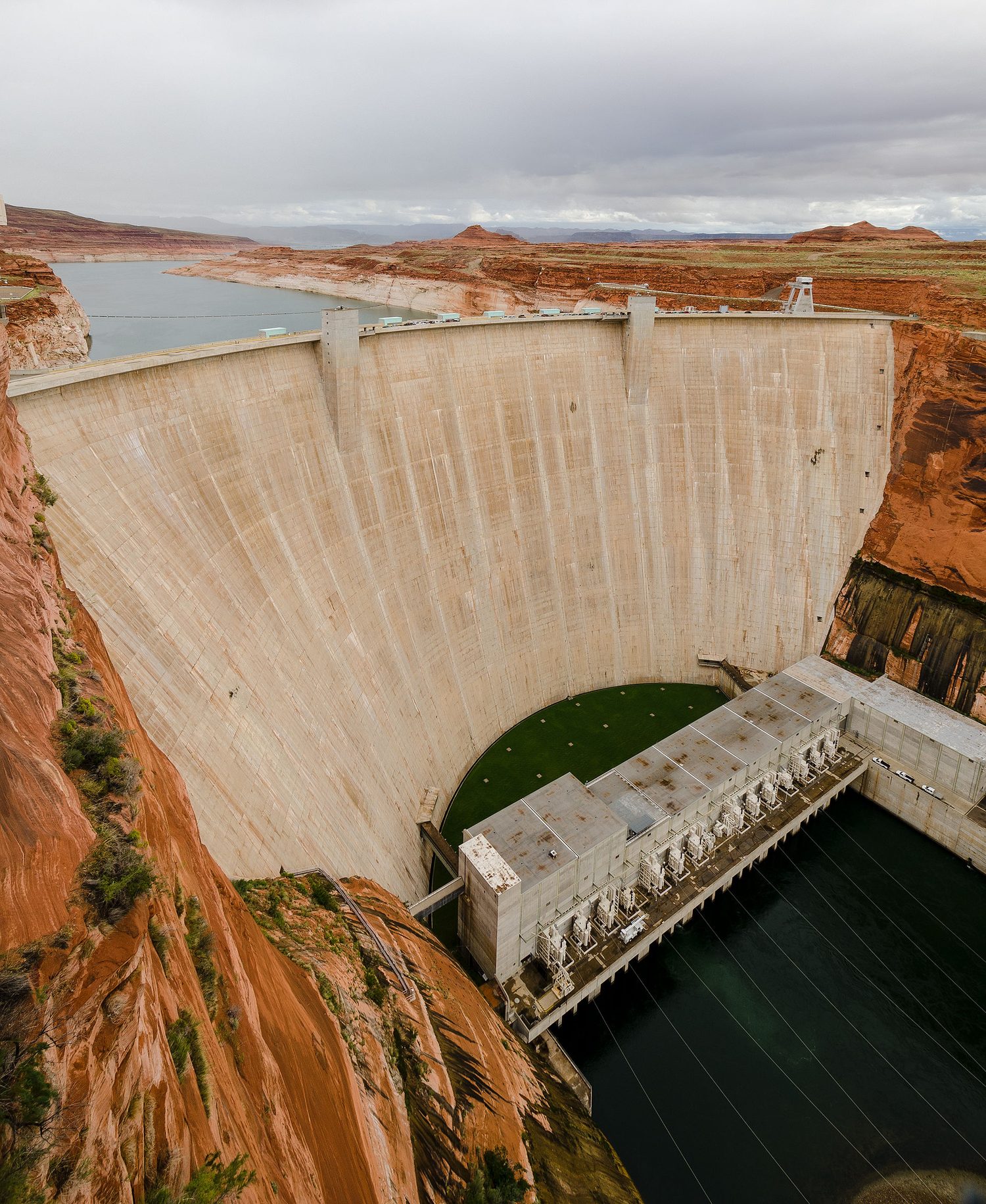 A tall concrete dam in a canyon: a full reservoir behind the curved wall, and the power house at the base where water is released