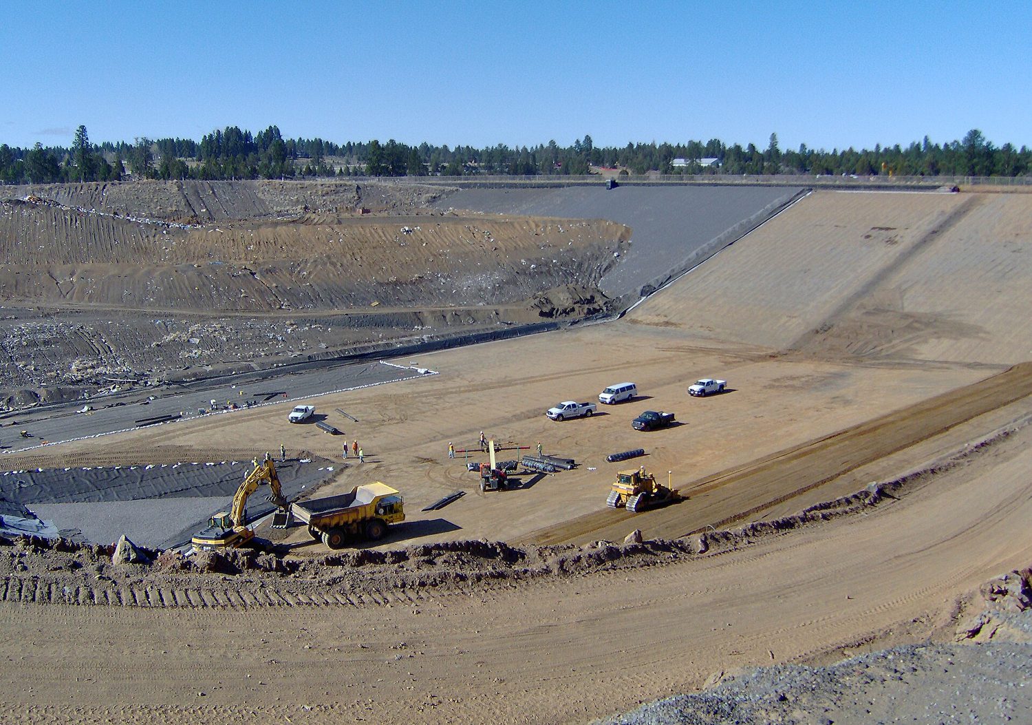 A large landfill mound of buried waste rising above a town in the valley below