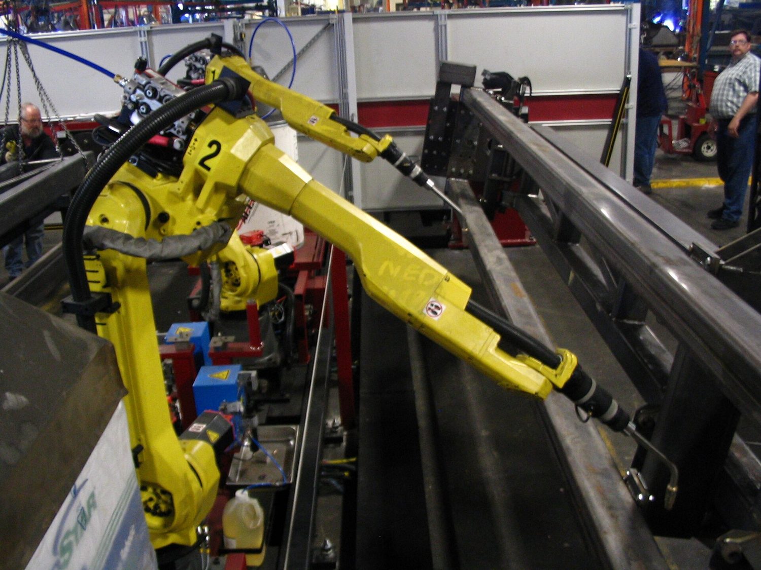 Several bright yellow robotic arms welding metal parts on an automated production line