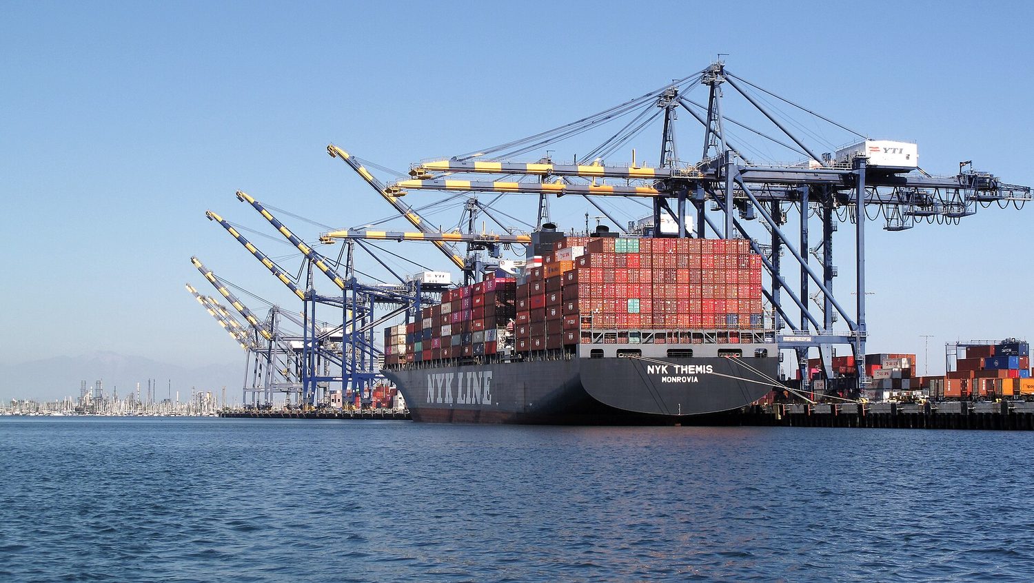 A huge container ship being unloaded by tall gantry cranes at a busy port