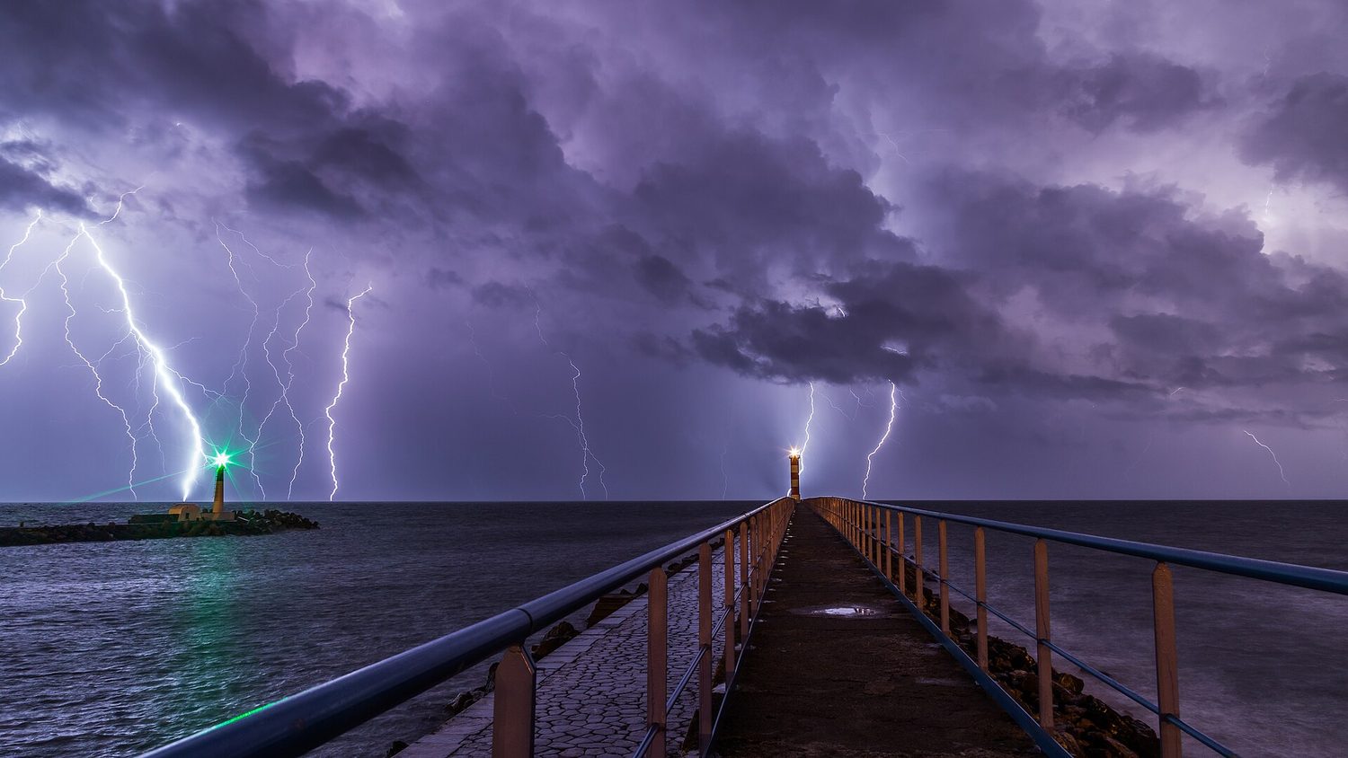 Several bright branching lightning bolts striking down from a stormy sky over a harbour