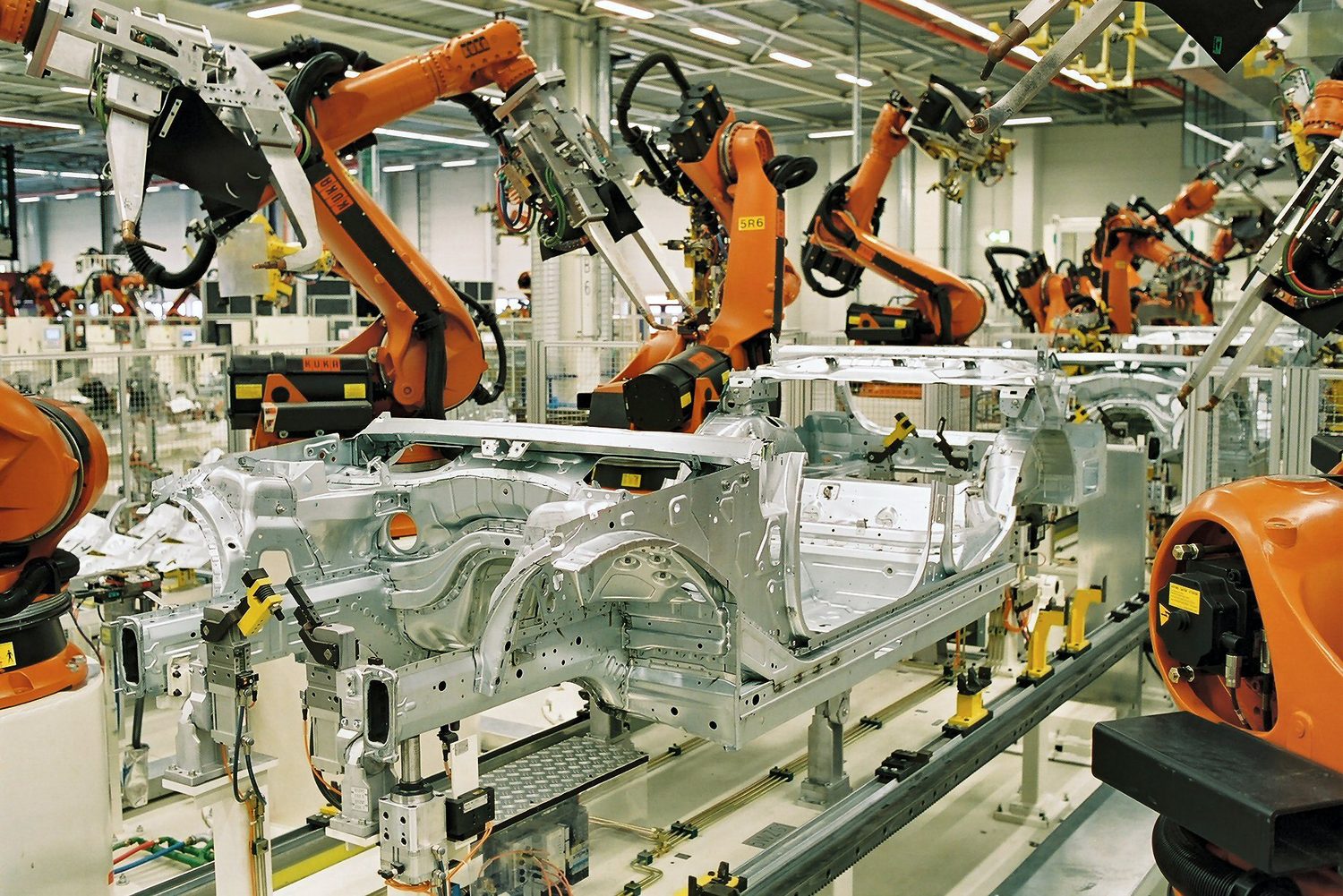 Orange robot arms welding a bare car body shell on an automated production line
