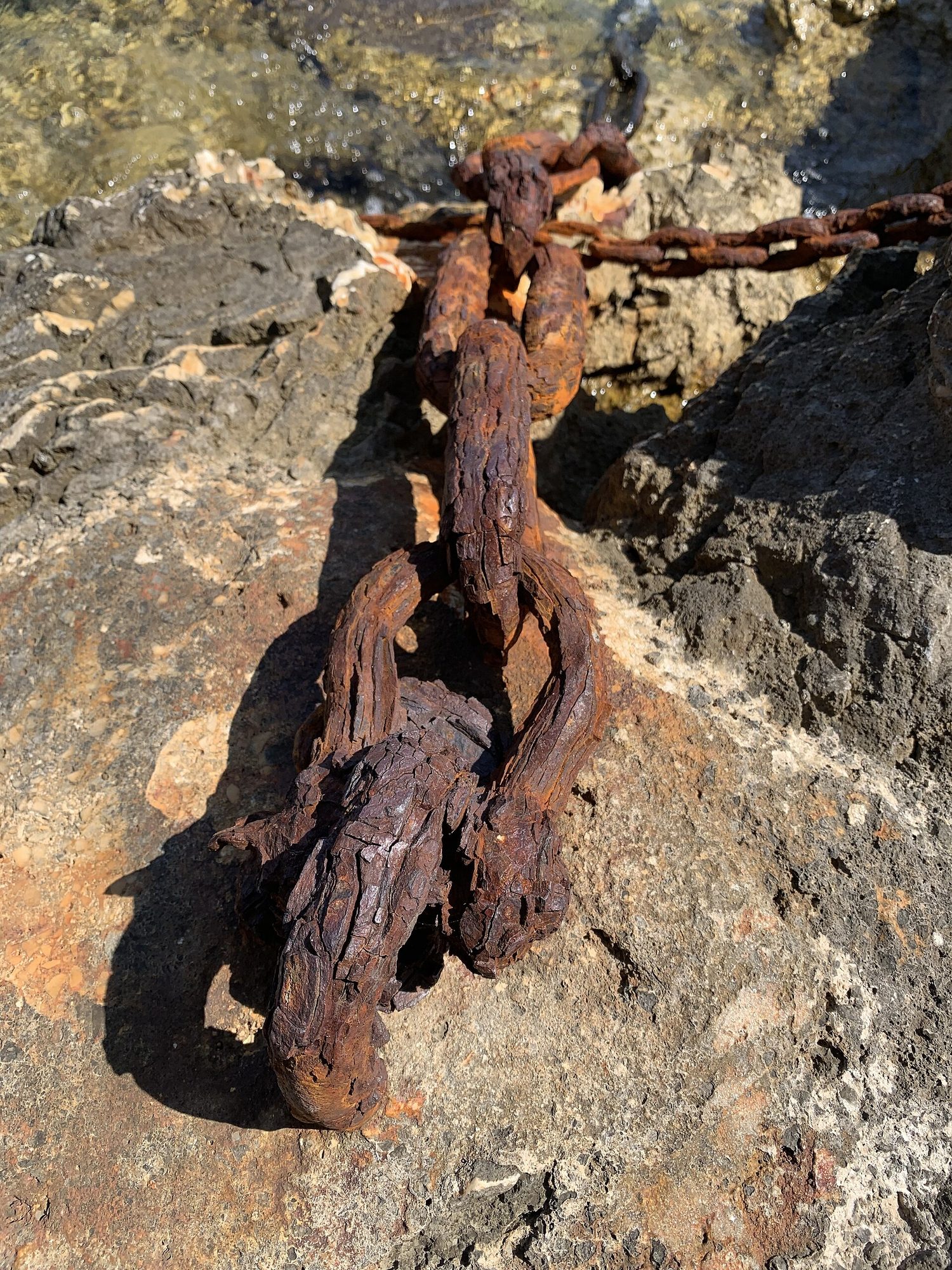 A heavy iron chain on coastal rocks, deeply covered in orange-brown rust