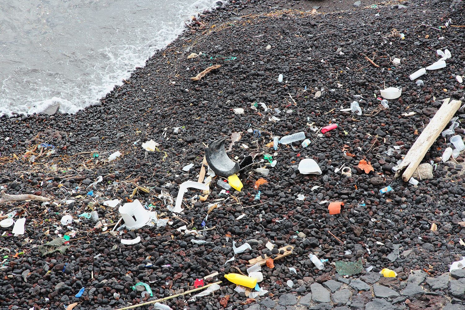 A pebble beach covered in washed-up plastic bottles, cups and broken plastic fragments