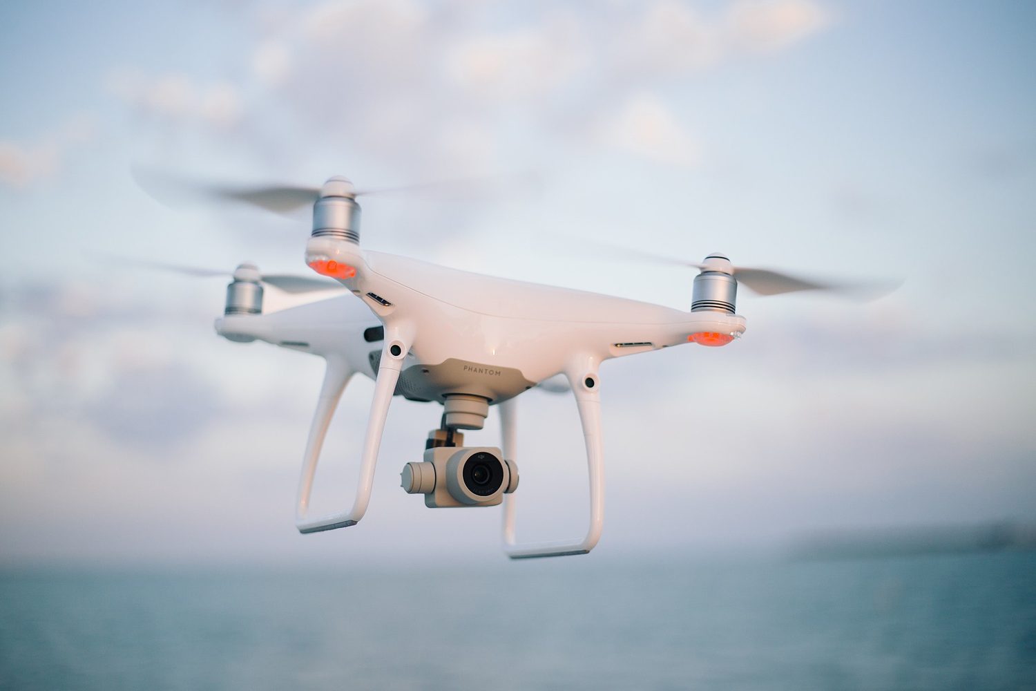A white four-rotor drone with a small camera, flying in the sky above the sea