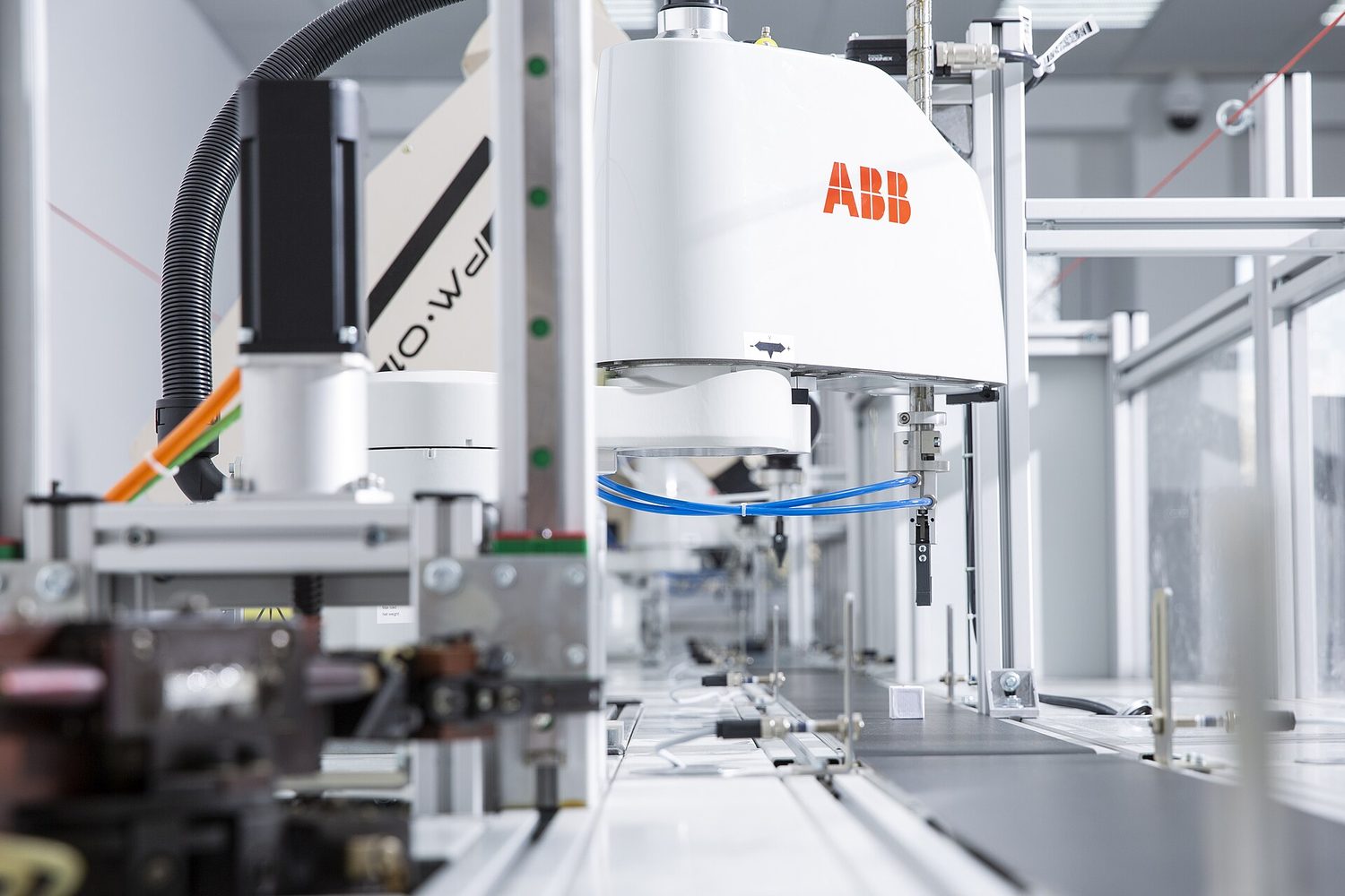 A white robot arm on a factory production line, with cables and metal framework around it