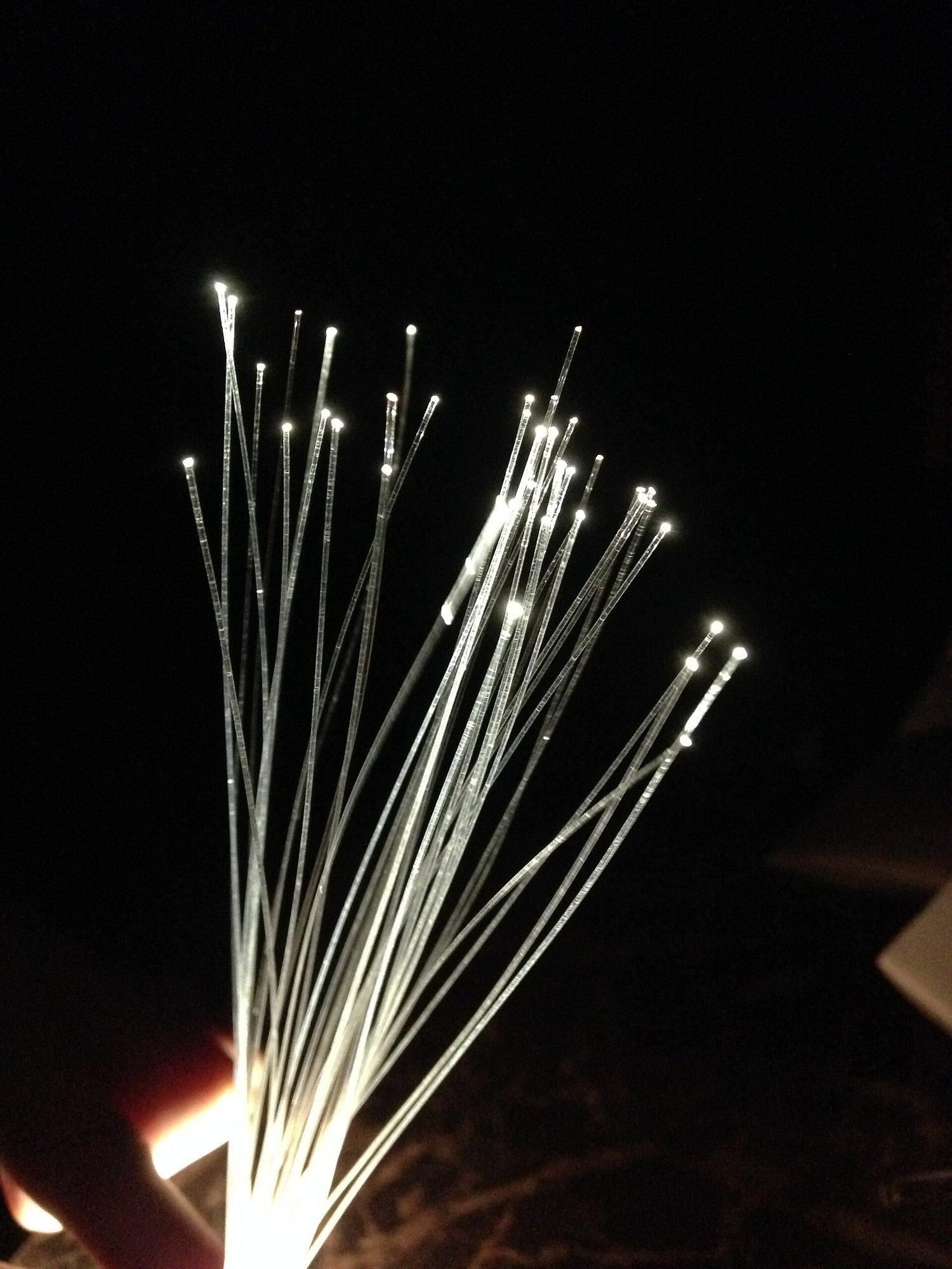 A bunch of thin fibres held in a hand, each one glowing brightly at its tip in a dark room